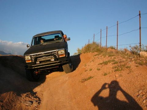 1984 Ford Bronco - A dark SUV navigates a dirt path on a sunny day, with a fence line visible on the hill.