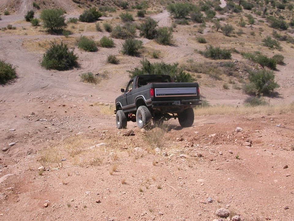 Rear view of dark 1980s Ford Bronco driving off-road