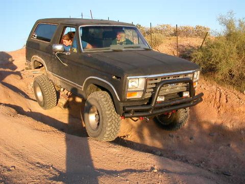 1984 Ford Bronco - 1984 Ford Bronco navigates a dusty off-road path under a clear sky.