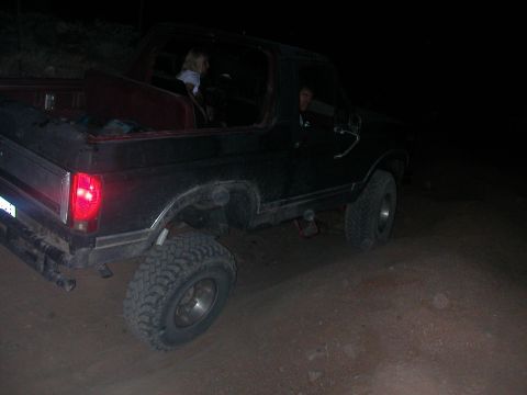 1984 Ford Bronco - A black Ford Bronco with aftermarket wheels and tires is viewed from the rear three-quarter angle in the dark.
