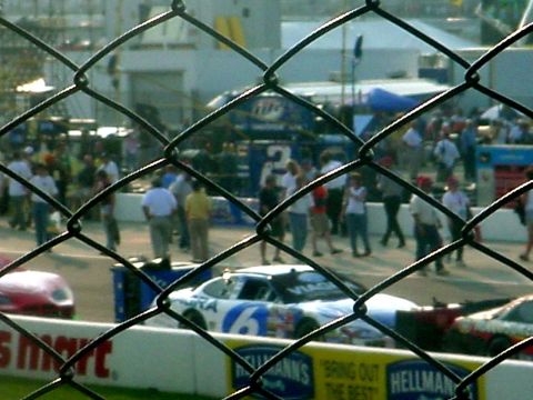 1973 Ford Ranchero - Stock cars are lined up on a race track, viewed through a chain-link fence.