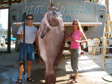 1973 Ford Ranchero - A couple proudly displays a massive fish caught and hoisted for display, with a boat named 'HEAD HUNTER' in the background.