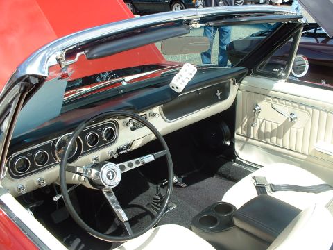 1999 Ford Crown Victoria - Interior view of a classic red convertible, likely a 1965 Ford Mustang, with a white interior and a prominent Mustang emblem on the steerin…