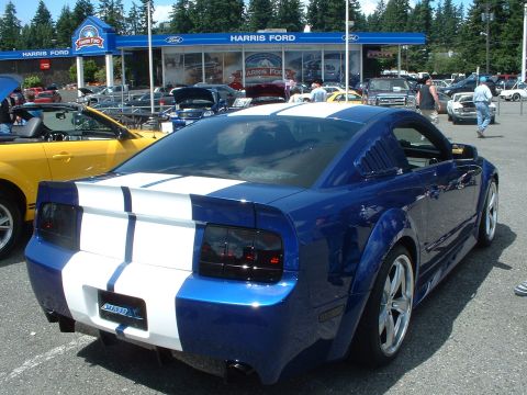 1999 Ford Crown Victoria - A blue 2005 Ford Mustang with white racing stripes is parked at Harris Ford.