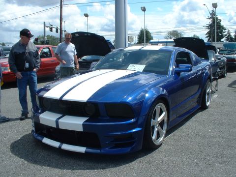 1999 Ford Crown Victoria - A blue Ford Mustang with white stripes is parked outside with two men standing next to it.