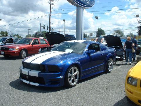 1999 Ford Crown Victoria - Blue Ford Mustang with white stripes on display at a Ford dealership.