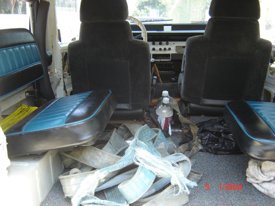 Interior of a vehicle with black seats and blue accents, straps and bottles on the floor