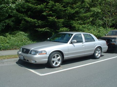 1999 Ford Crown Victoria - Silver sedan parked in a parking spot with a brown SUV beside it.