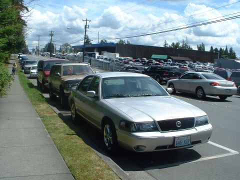 1999 Ford Crown Victoria - A silver sedan is parked curbside on a street with a lot of other vehicles in the background.
