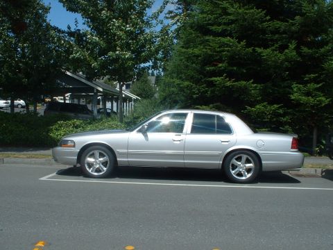 1999 Ford Crown Victoria - Silver sedan with chrome wheels and tinted windows parked on asphalt.