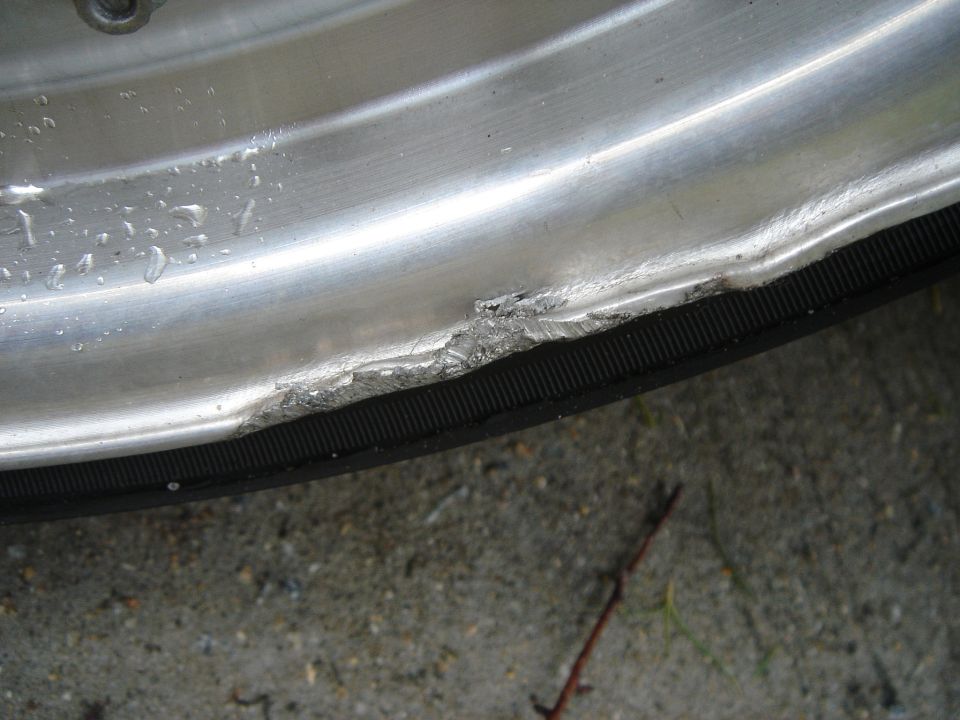 Damaged aluminum wheel rim with tire, showing significant dents and scrapes along the edge