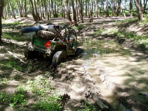 1992 Ford Bronco - A person is lying on the spare tire of an off-road vehicle that is stuck in a muddy water-filled ditch.