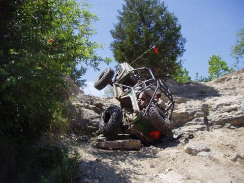 1992 Ford Bronco - An off-road vehicle navigates a steep, rocky terrain, tilted precariously on its side.