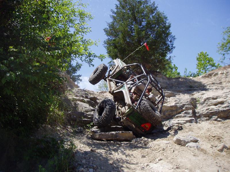 Off-road vehicle tilted on rocky incline with roll cage and large tires