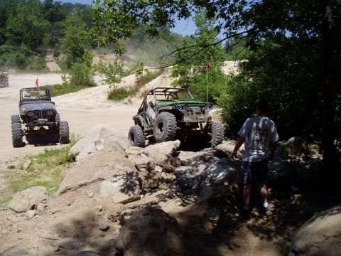 1992 Ford Bronco - Off-road vehicles tackle a challenging rocky trail with trees and dirt hills in the background.