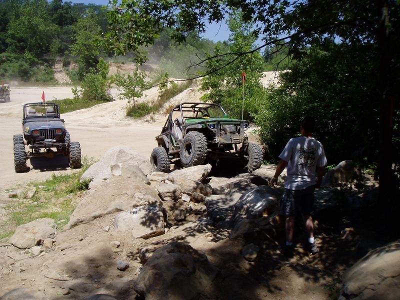 Two modified Jeeps navigating a rocky off-road course. One is dark colored, the other is green with a roll cage