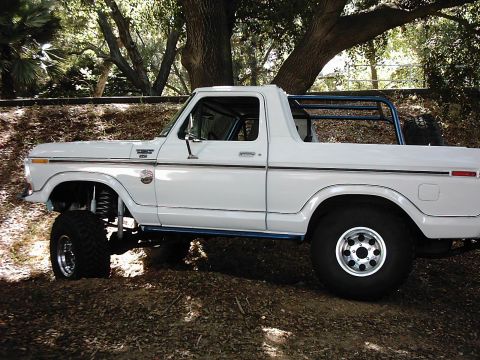 1978 Ford Bronco - Side view of a lifted 1978 Ford Bronco with a roll cage, parked in a wooded area.