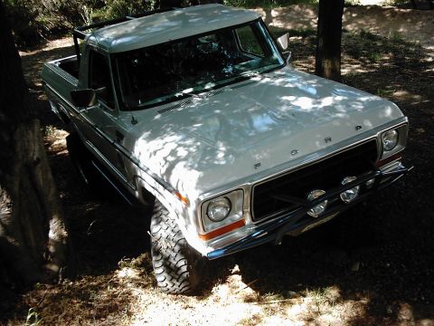 1978 Ford Bronco - This white Ford pickup truck is parked off-road, surrounded by trees and dappled sunlight.