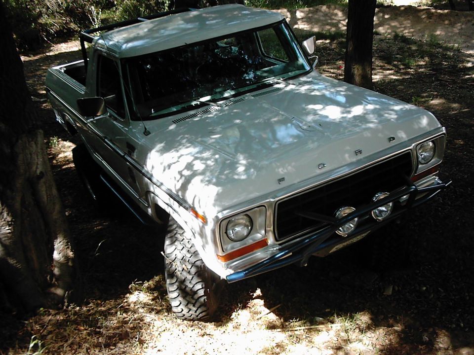 White Ford pickup truck parked among trees. Has a brush guard with lights