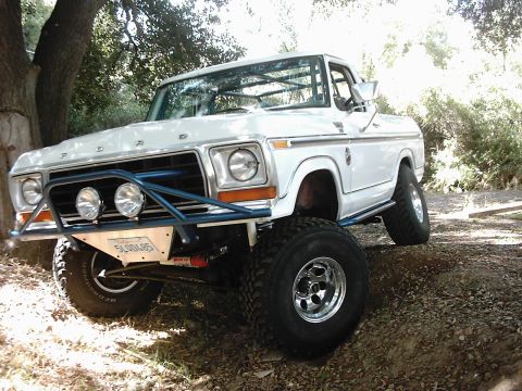 1978 Ford Bronco - A white 1978 Ford Bronco is modified for off-road use with a prominent blue bumper and roll cage.