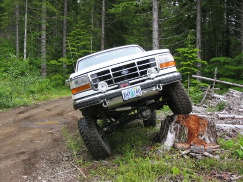 1995 Ford Bronco - This lifted Ford truck is navigating an obstacle on a wooded trail.