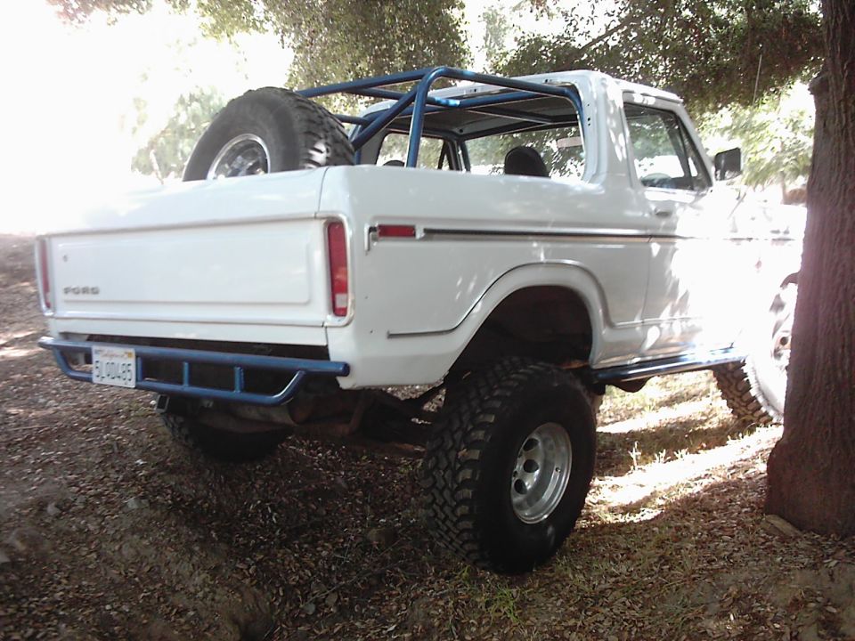 White 1978 Ford Bronco with blue roll cage and aftermarket bumper, parked outdoors
