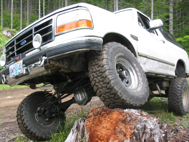 White lifted Ford Bronco on mud tires climbing a tree stump in the woods