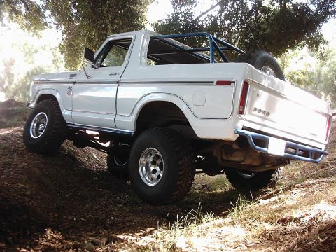 1978 Ford Bronco - 1978 Ford Bronco shown climbing a dirt incline with a roll cage and spare tire visible.