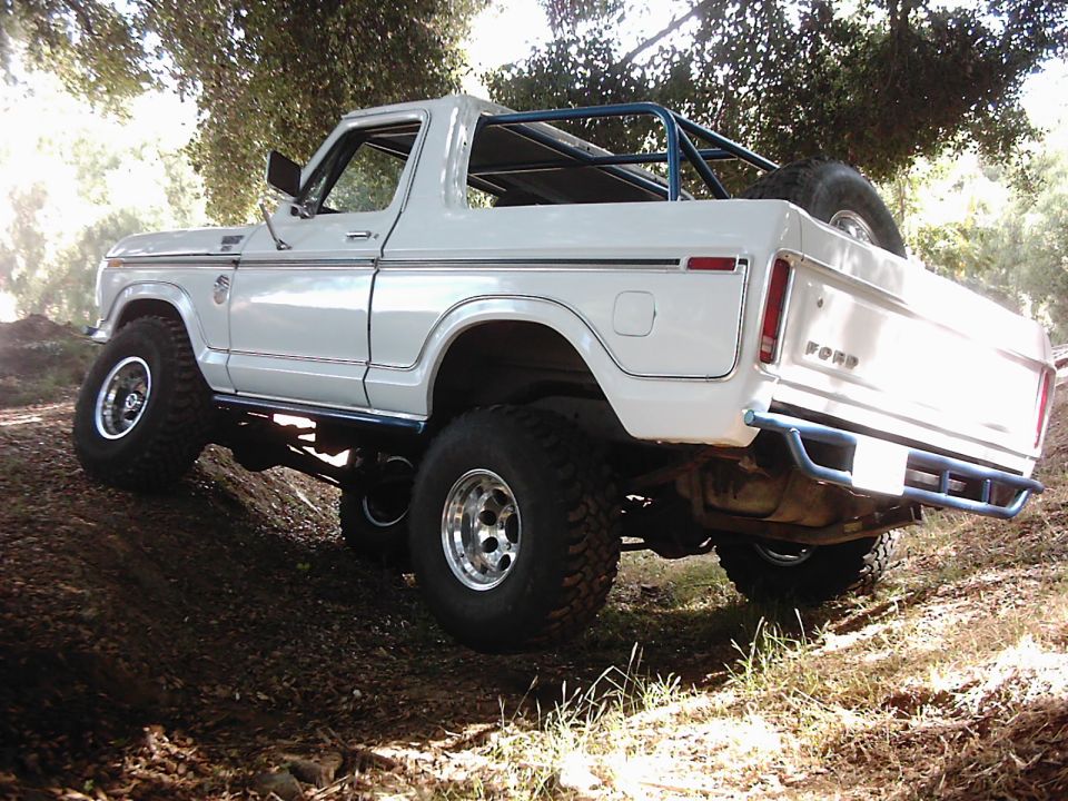 White 1978 Ford Bronco with roll cage and spare tire on back, climbing a dirt hill