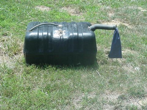 1988 Ford Bronco - A detached fuel tank rests on the grass, its hose capped with a blue rag.