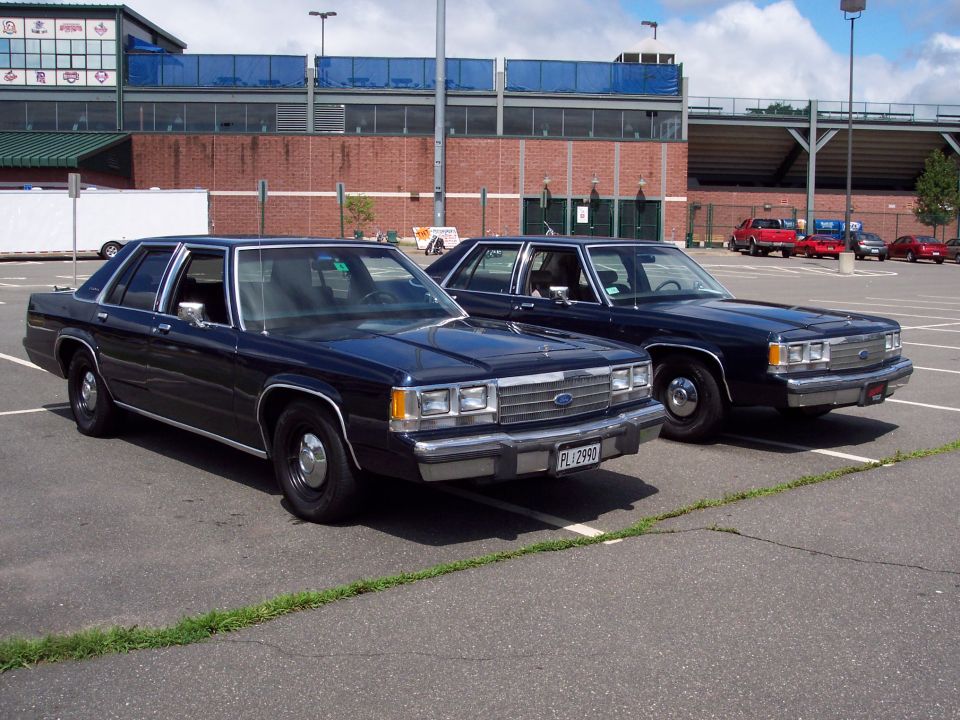 Two dark Ford LTD Crown Victoria sedans parked side by side in stadium lot