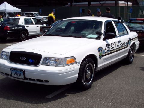 2001 Ford Crown Victoria - A white 2001 Ford Crown Victoria police car is parked at an event, with another police car visible behind it.