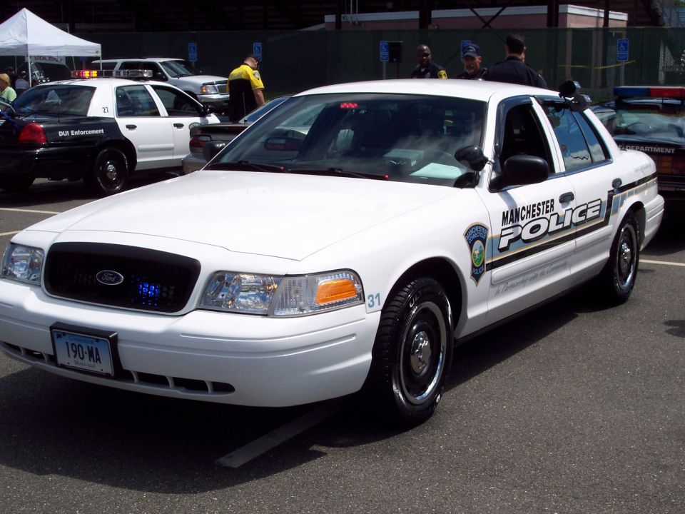 White 2001 Ford Crown Victoria police car with 'MANCHESTER POLICE' text, parked on asphalt