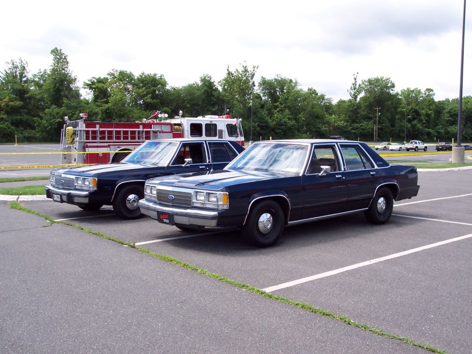 Two dark blue police sedans parked side-by-side, front view