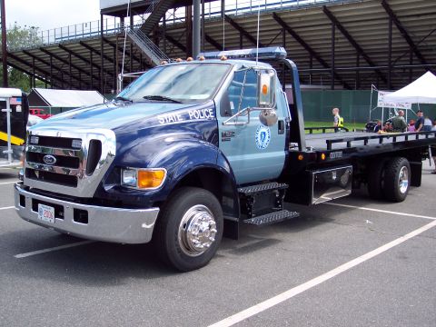 2001 Ford Crown Victoria - A blue and gray Ford F-series tow truck is parked on asphalt, with stadium seating in the background.