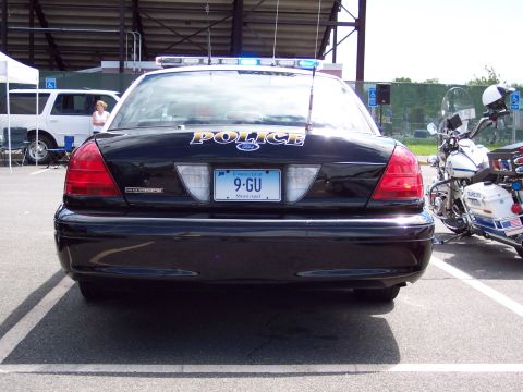 2001 Ford Crown Victoria - A black 2001 Ford Crown Victoria police car is seen from the rear, parked next to a police motorcycle.