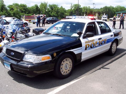 2001 Ford Crown Victoria - A black and white police car with flashing lights is parked at an outdoor event.