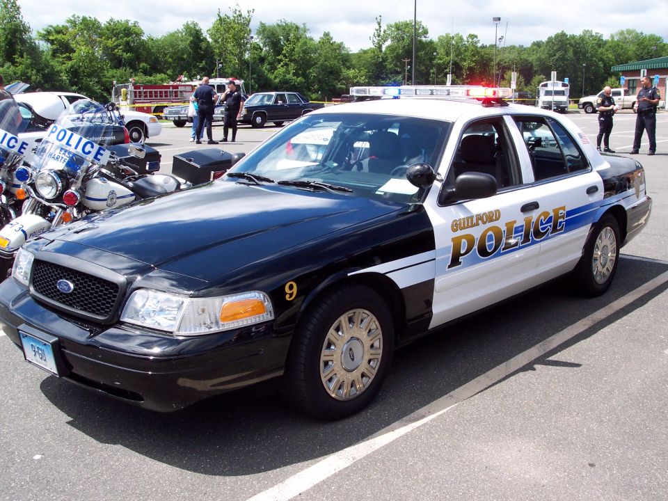 Ford Crown Victoria police car with 'GUILFORD POLICE' on the side, parked next to motorcycles