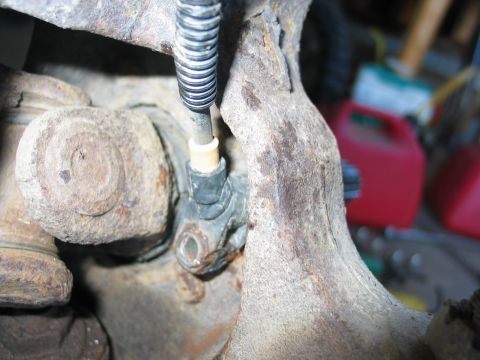 1995 Ford Bronco - Tight close-up under a vehicle showing a heavily rusted cast steering knuckle and axle U-joint, with a spring-wrapped flexible line running…