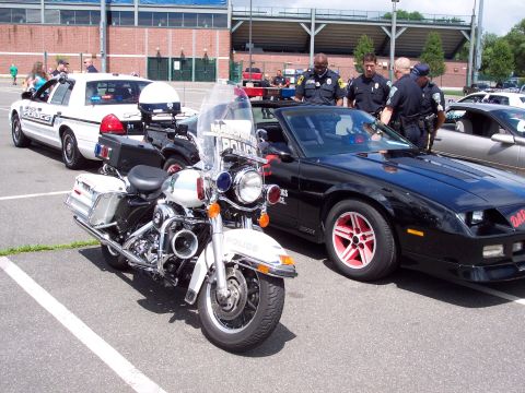 2001 Ford Crown Victoria - A police motorcycle and a black convertible are parked together, with officers standing nearby.
