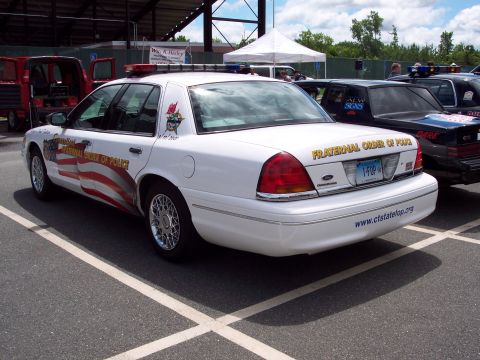 2001 Ford Crown Victoria - A white 2001 Ford Crown Victoria police car is parked in a lot next to other vehicles.