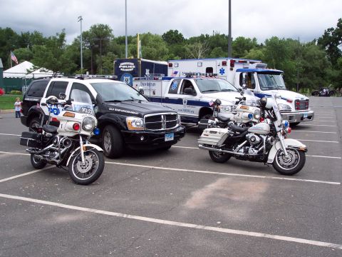 2001 Ford Crown Victoria - Several law enforcement and emergency vehicles are parked in a lot, including motorcycles, an SUV, an ambulance, and a truck.
