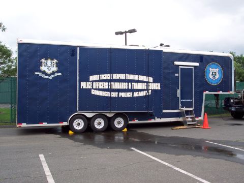 2001 Ford Crown Victoria - A blue trailer labeled for police training is parked on a wet asphalt lot.