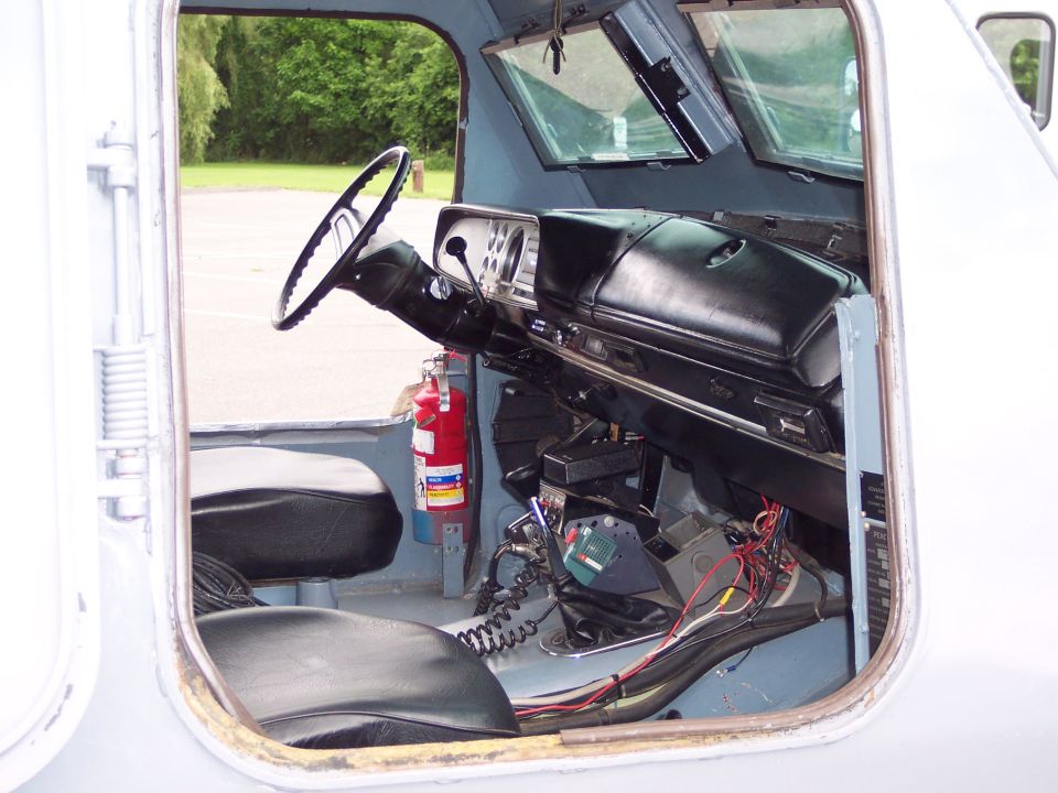Interior view of a vehicle showing a steering wheel, dashboard, fire extinguisher, and exposed wiring