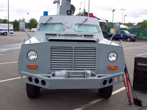 2001 Ford Crown Victoria - Armored truck with winch and emergency lights parked in a lot. Another vehicle is visible in the background.