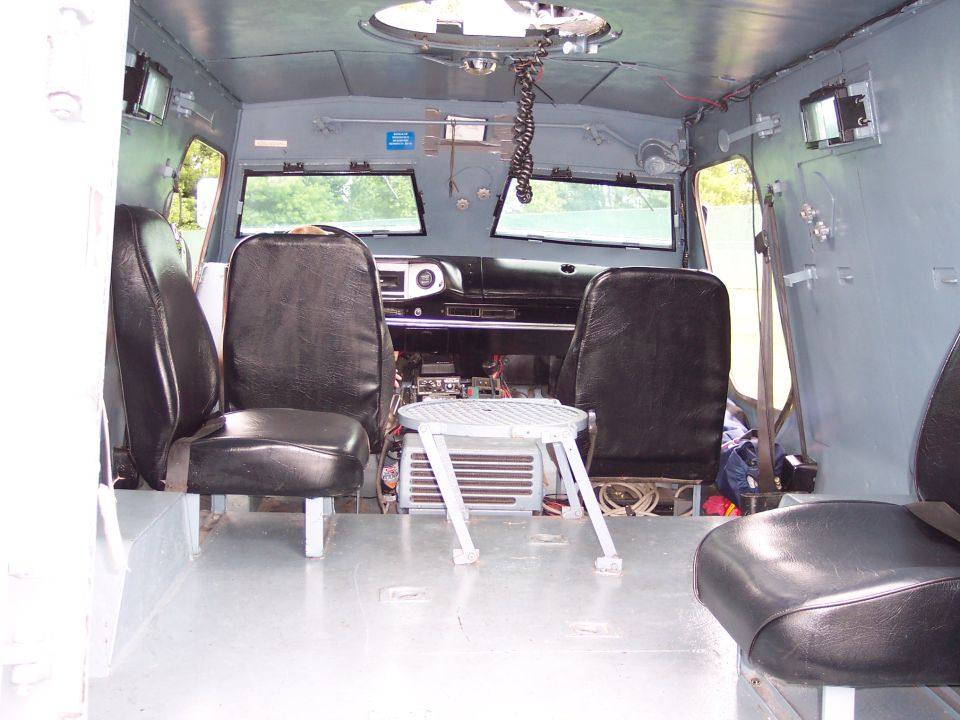 Interior view of a gray vehicle with black vinyl seats, a dashboard with two windows, and a portable stool