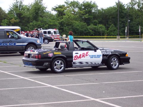 2001 Ford Crown Victoria - A black and white convertible police car, marked with D.A.R.E. livery, is parked in a lot alongside other vehicles.