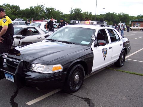 2001 Ford Crown Victoria - A police car with its lights on is parked in a lot, with several officers standing nearby.