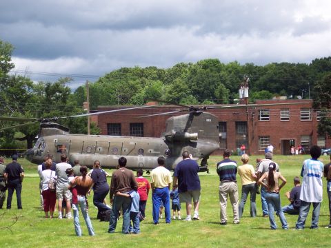 2001 Ford Crown Victoria - A crowd gathers to view a large military helicopter parked on a field near a brick building.