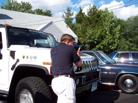 2001 Ford Crown Victoria - A white Hummer H2 police SUV is parked next to a dark sedan, with a person taking a photo.
